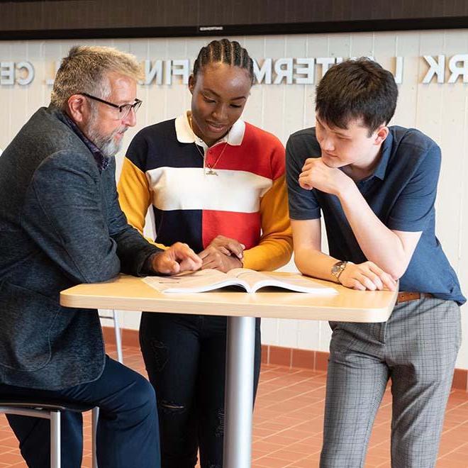 Professor and two business students looking at textbook